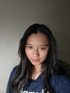 Portrait of Jane with long dark hair wearing a navy shirt, facing the camera against a plain wall.